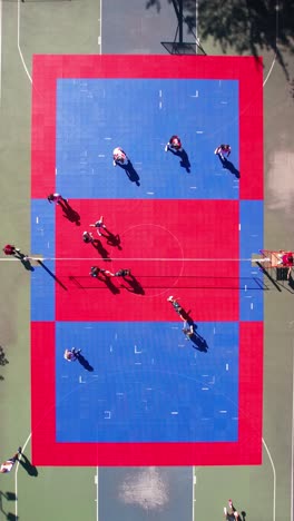 vertical drone shot of people playing volleyball on sunny outdoor court, birdseye aerial view