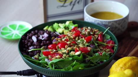 adding salad dressing on plate of salad on rotating platform black beans pumpkin seeds avocado spinach tomatoes salad dressing lemons