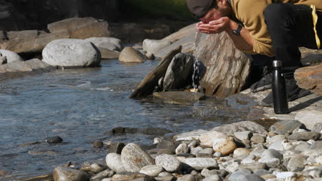 man drinks fresh river water using hands on his knees