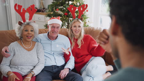 Adult-Family-Sitting-On-Sofa-Playing-Game-Of-Charades-At-Christmas-Together