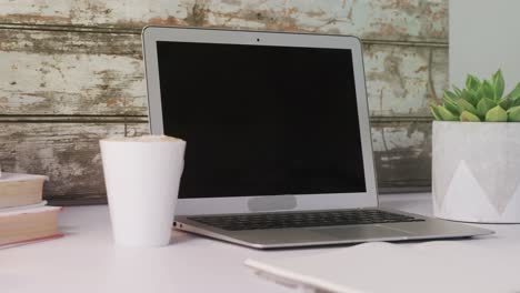 archivos, planta de aloe vera, computadora portátil y una taza de café en la mesa