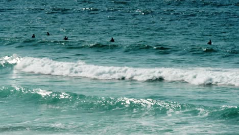 Groups-of-surfers,-paddling-in-the-water-waiting-for-the-surf-off-the-coast-in-Cornwall,-UK