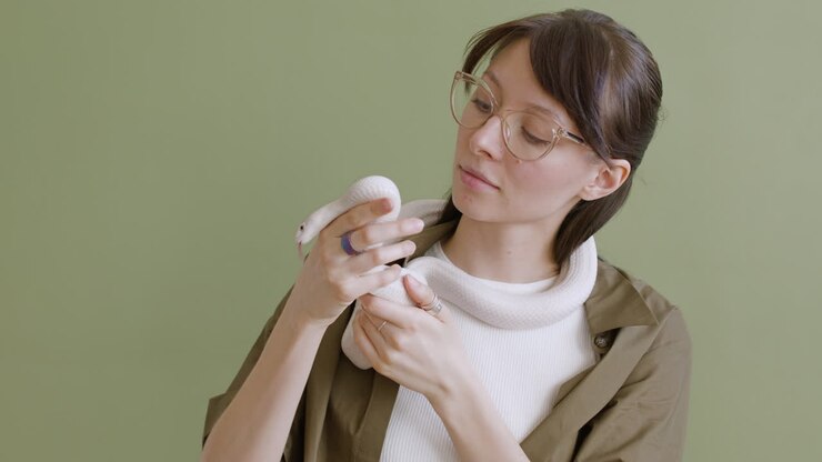 Portrait Of A Young Woman With Eyeglasses Holding A White Pet Snake Around Her Neck And Hands On A Green Background 1