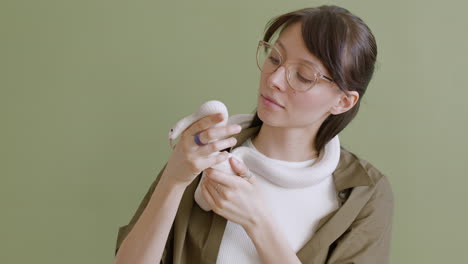 portrait of a young woman with eyeglasses holding a white pet snake around her neck and hands on a green background 1