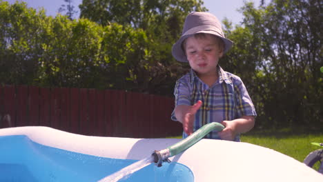 little boy spraying water into a pool with a hose