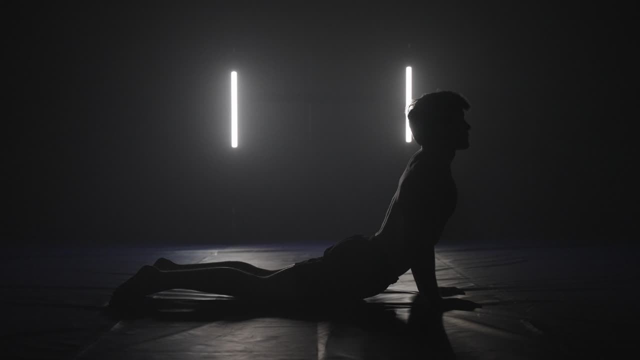Sfinks yogastilling udført af en mandlig atlet i et mørkt studie, silhuet yogastilling.