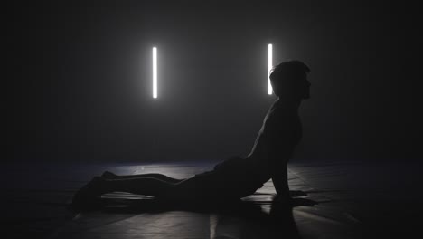 sphinx yoga pose performed by male fighter in dark studio, silhouette yoga pose