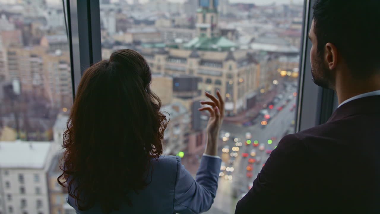 una pareja de compañeros de trabajo discutiendo la arquitectura de la ciudad mirando de cerca la ventana de la oficina.