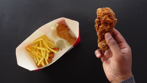 person holding a fried chicken drumstick with a box of french fries and chicken tenders