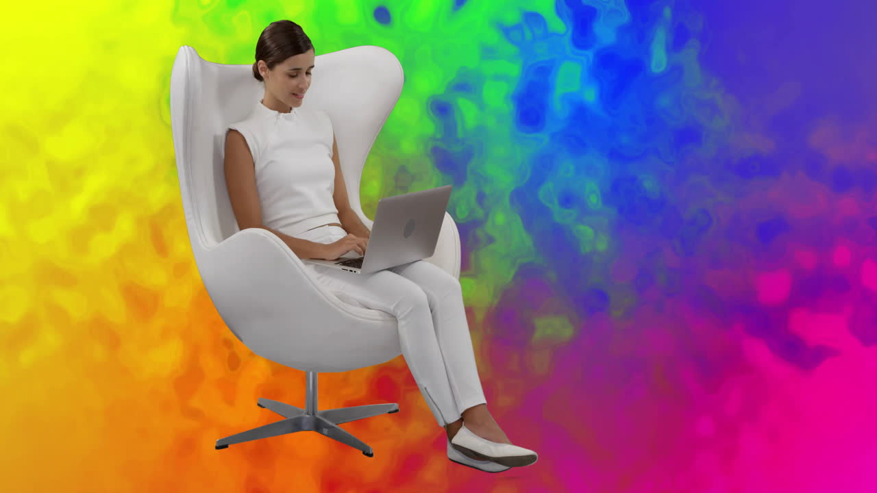 Using laptop in modern chair, woman in animation studio with rainbow background