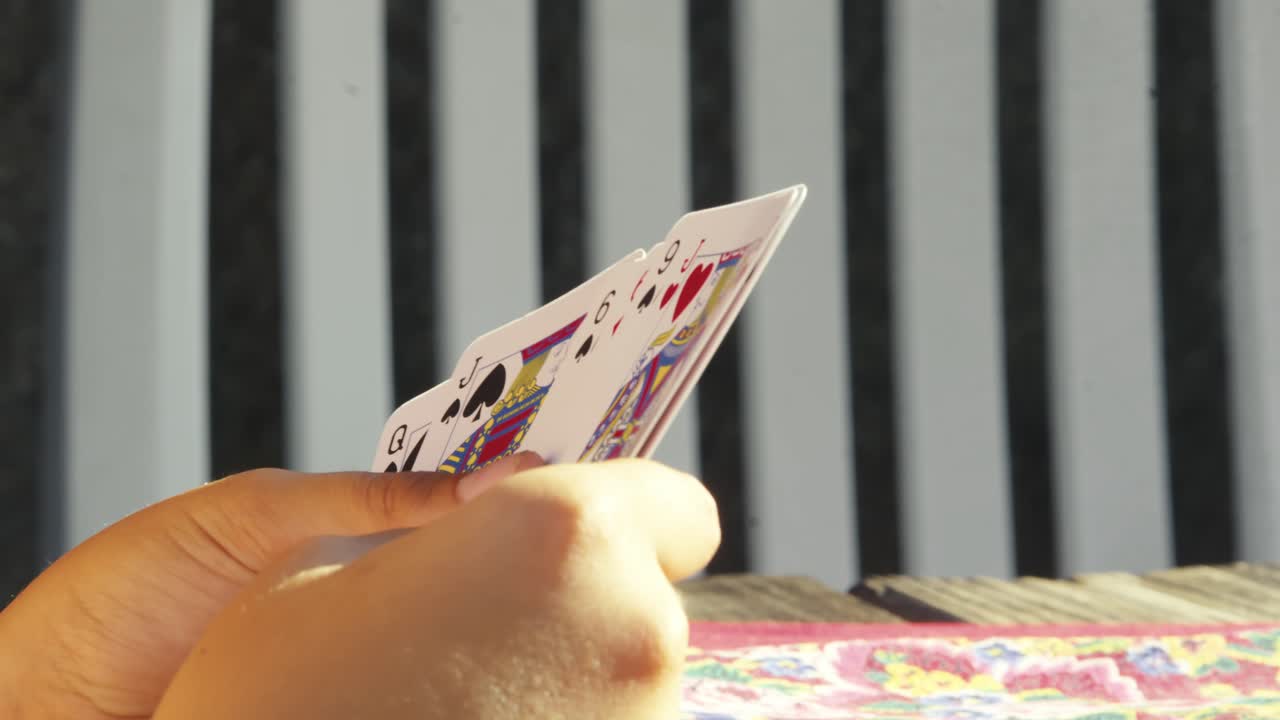 Young Hands display playing cards at sunny outdoor friendly table game