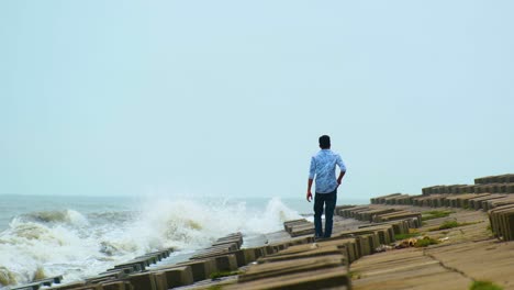 Un-Hombre-Solitario-Encendiendo-Un-Cigarrillo-Mientras-Caminaba-Por-La-Costa-Con-Un-Rompeolas-De-Piedra-En-Bloque