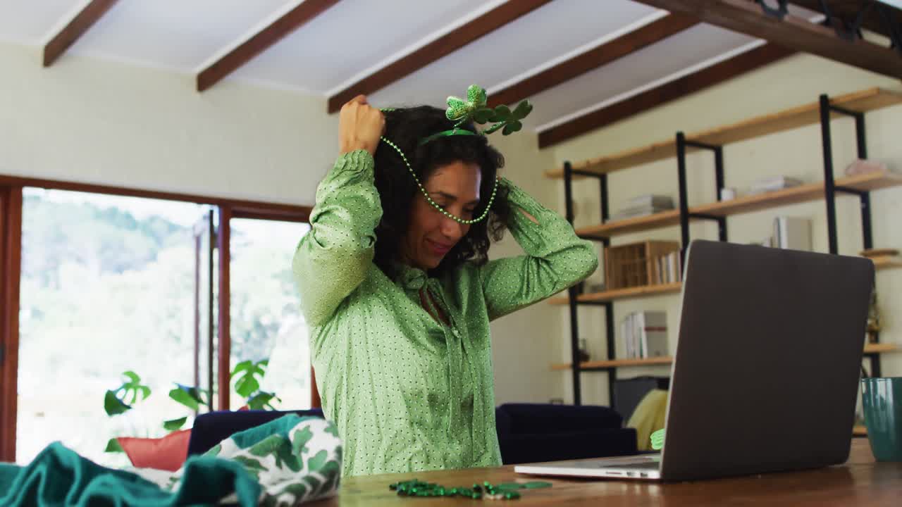 Mixed race woman in green beads necklace and costume having a video call on laptop at home