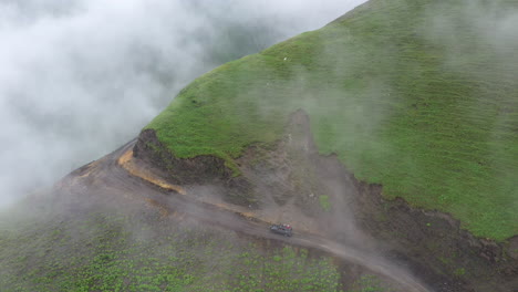 Descending-drone-shot-of-vehicle-driving-on-the-edge-of-a-cliff-on-the-Road-to-Tusheti,-one-of-the-worlds-most-dangerous-roads