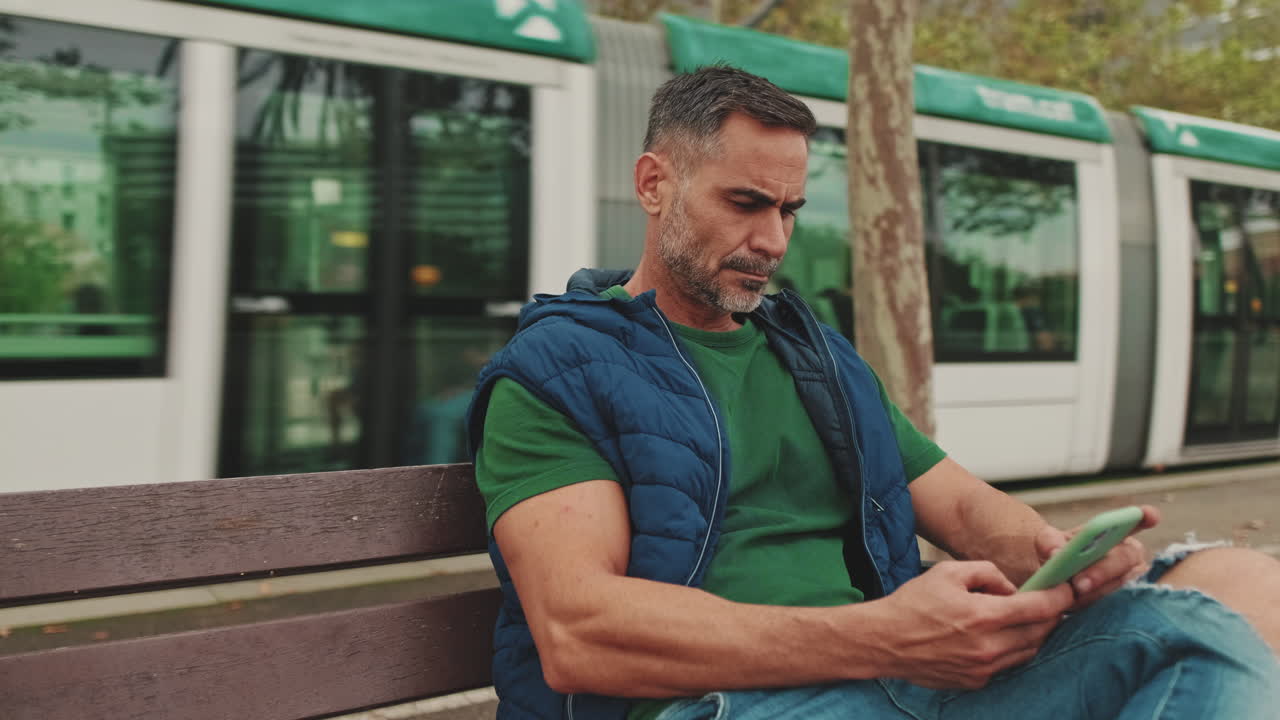Man sitting on a bench using his phone in a city park