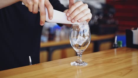 transparent glass with ice cubes. bartender is putting crystal ice cubes in a glass before preparing an alcoholic cocktail to customers on the bar table.