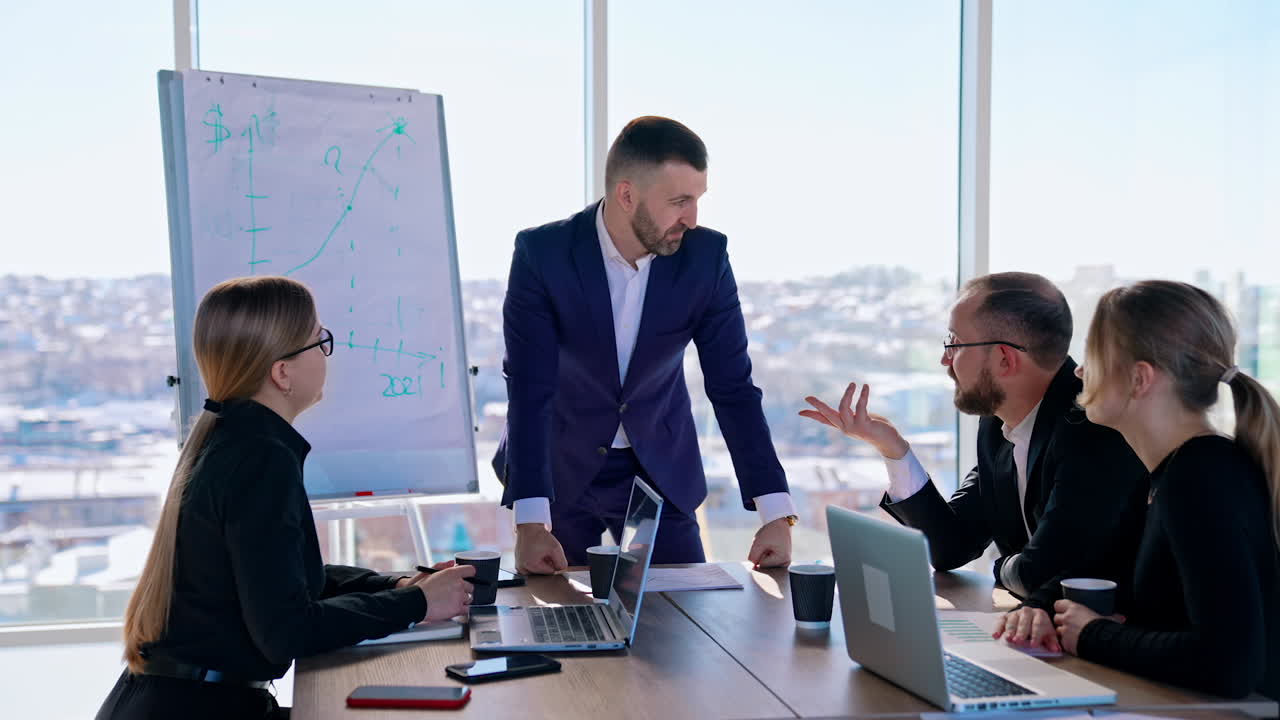 Business colleagues discuss new blueprint in office. Young entrepreneurs sitting at the table and listen to successful businessman on large window background.