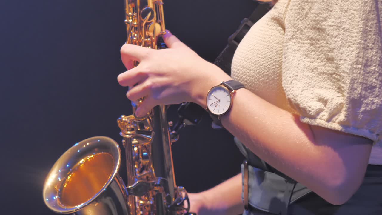 Primo piano di mani e dita femminili su un sassofono dorato che suona un assolo.