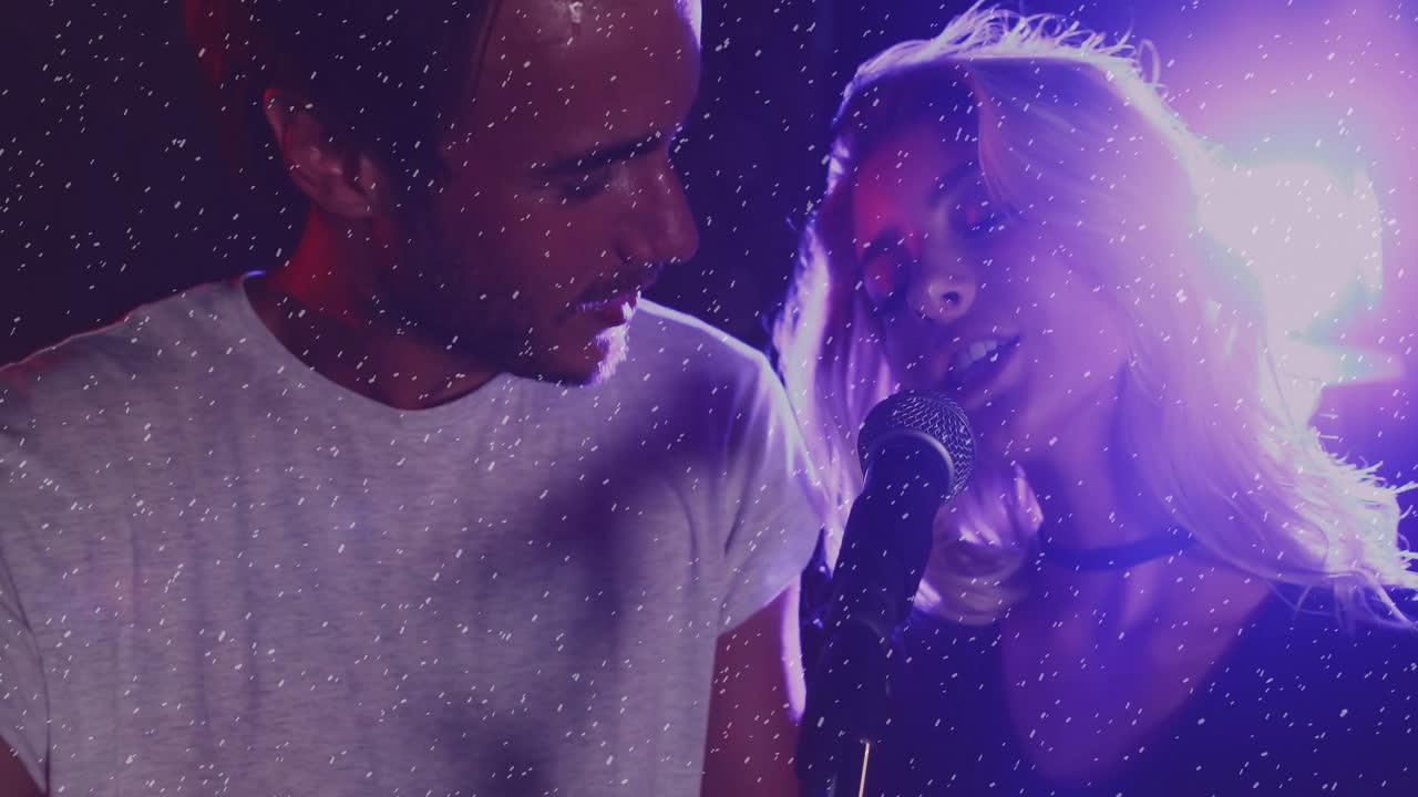 Music industry duo performing with microphone on stage, with snow particles and purple lighting