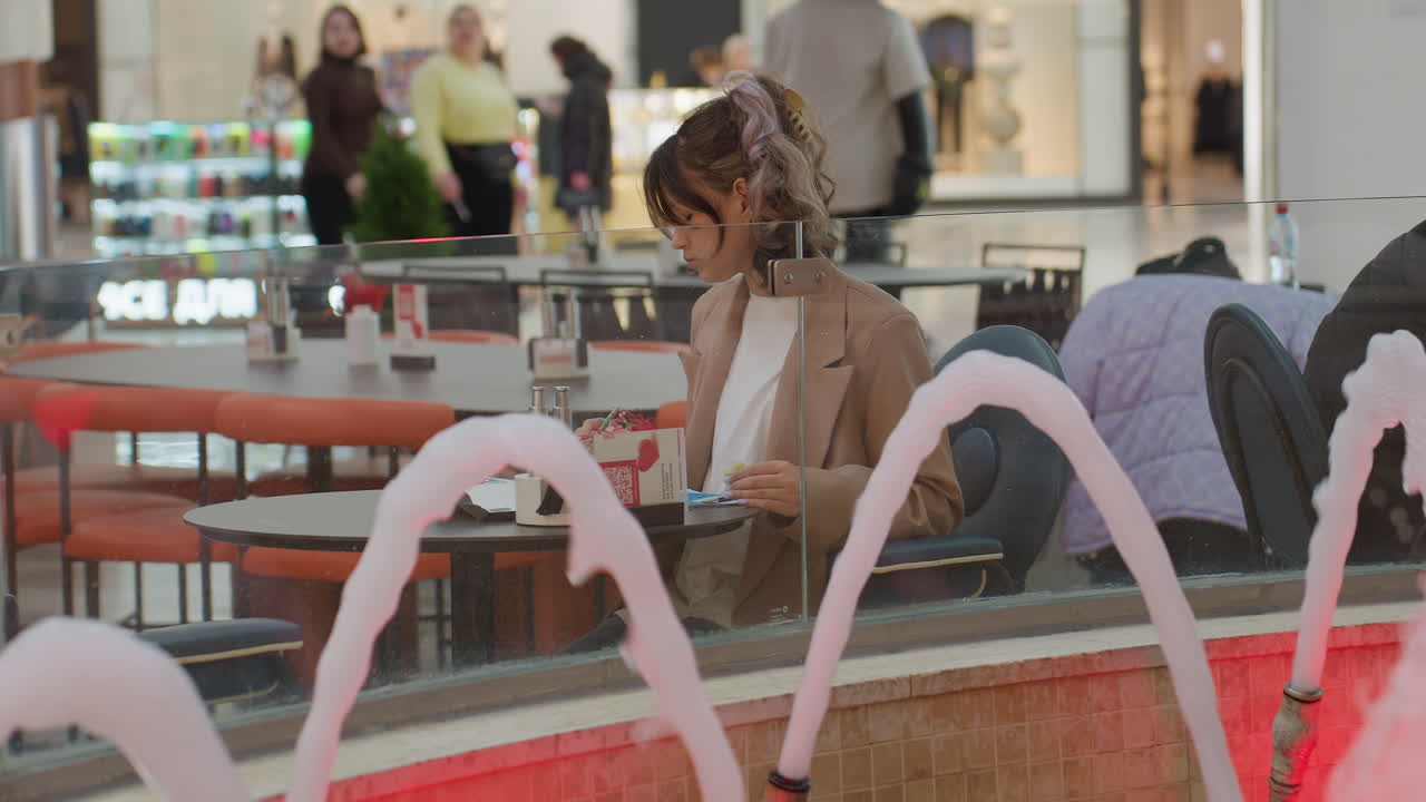 una observadora tranquila y serena se relaja en una concurrida zona comercial con llamativas fuentes de agua; una mujer serena descansa en silencio cerca de los surtidores de agua ornamentales en una ajetreada plaza comercial con coloridos reflejos