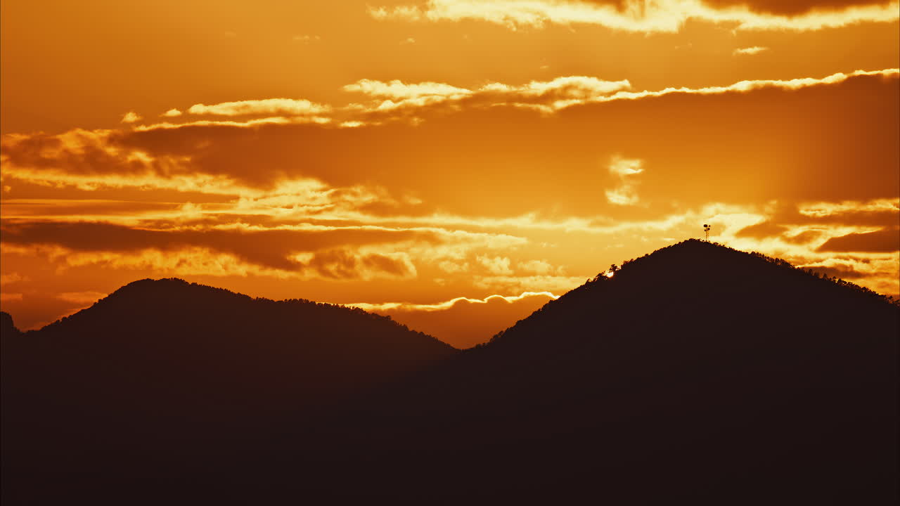 Distant view of a yacht docked on the sea with a mountain on the background at sunset