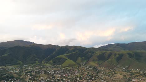 Aerial-view-of-the-Mountain-of-Tafi-del-Valle-at-sunset-with-the-city-in-the-front,-cloudy-sky,-slowmotion-and-copy-space