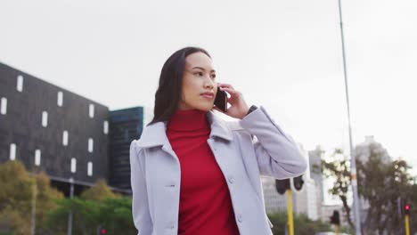 asian woman walking dragging suitcase and talking on smartphone