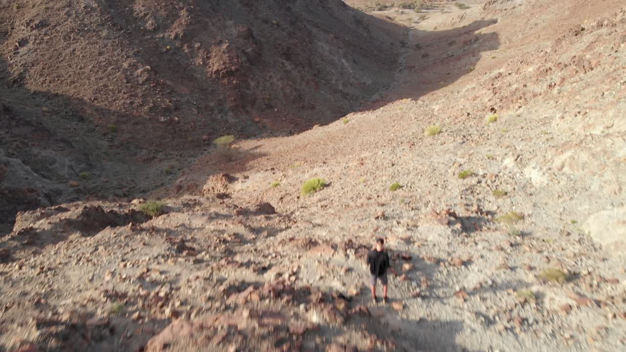 아랍 에미레이트 하타의 바위산 꼭대기에 서 있는 젊은 남성의 무인 항공기에서 공중 서사시 촬영