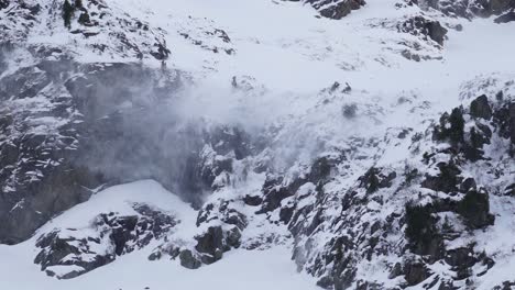 cerca de la nieve siendo soplado de una cresta de acantilado de montaña en un glaciar rocoso nevado