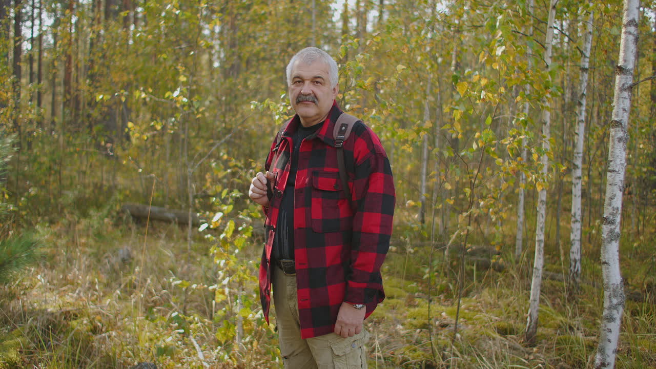 un hombre alegre de mediana edad está de pie en el bosque de otoño con árboles amarillentos durante el día sonriendo a la cámara excursionista y viajero