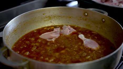 raw chicken poultry pieces being placed and cooked in simmering curry sauce in pot