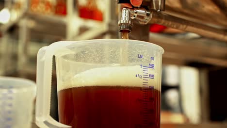 amber beer filling plastic measuring jug from tap in brewery production and quality control