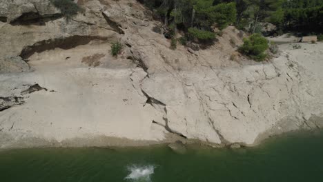 Panorama-Drohnenaufnahme-Eines-Jungen-Mannes,-Der-Vom-Rand-Eines-Felsens-In-Ein-Natürliches-Gewässer-Springt,-Mit-Bäumen-Im-Hintergrund,-Der-Urlaub-Auf-Einer-Solo-Reise-Nach-El-Chorro-Von-Málaga,-Spanien,-Genießt