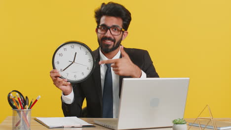 man in a suit holding a clock and pointing at a laptop