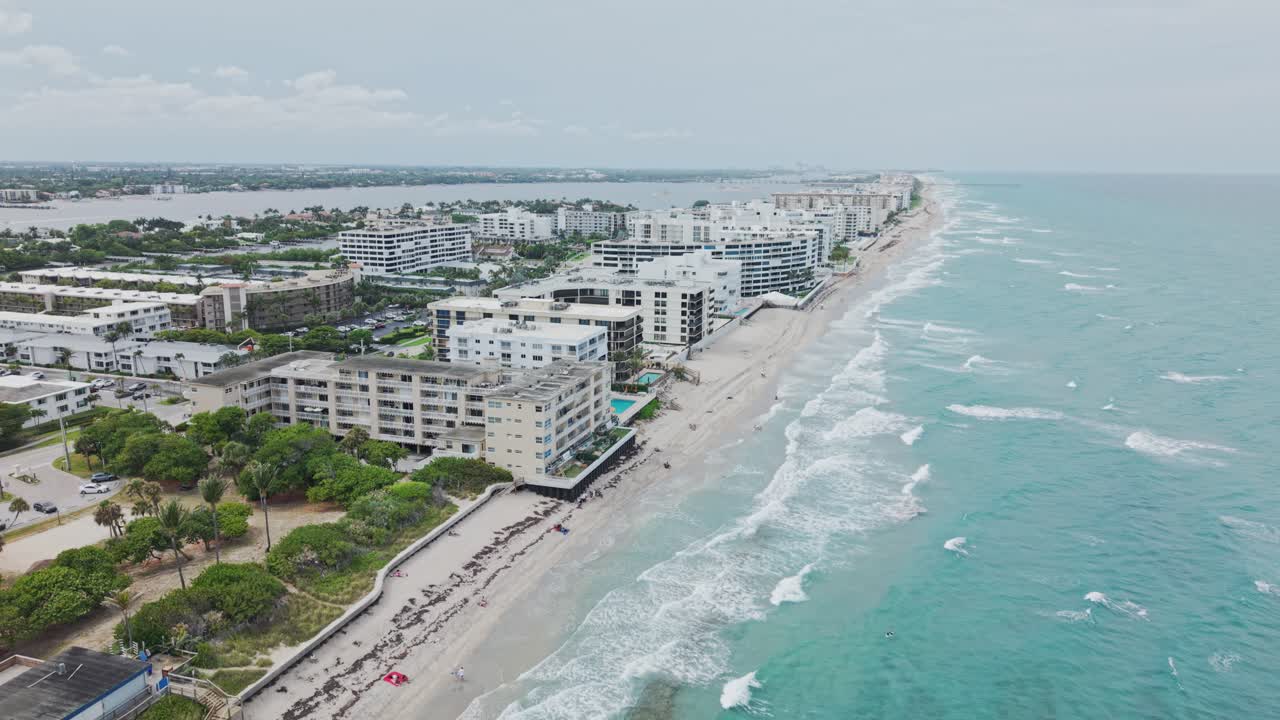 Jib down drone shot of beach and hotels next to Atlantic Ocean with cloudy weather during the day in West Palm Beach, Florida, USA