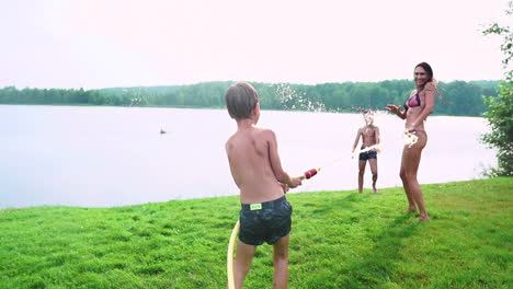 día soleado de verano en el césped familia con dos niños se divierten jugando con el agua y riendo. atmósfera alegre de una familia feliz
