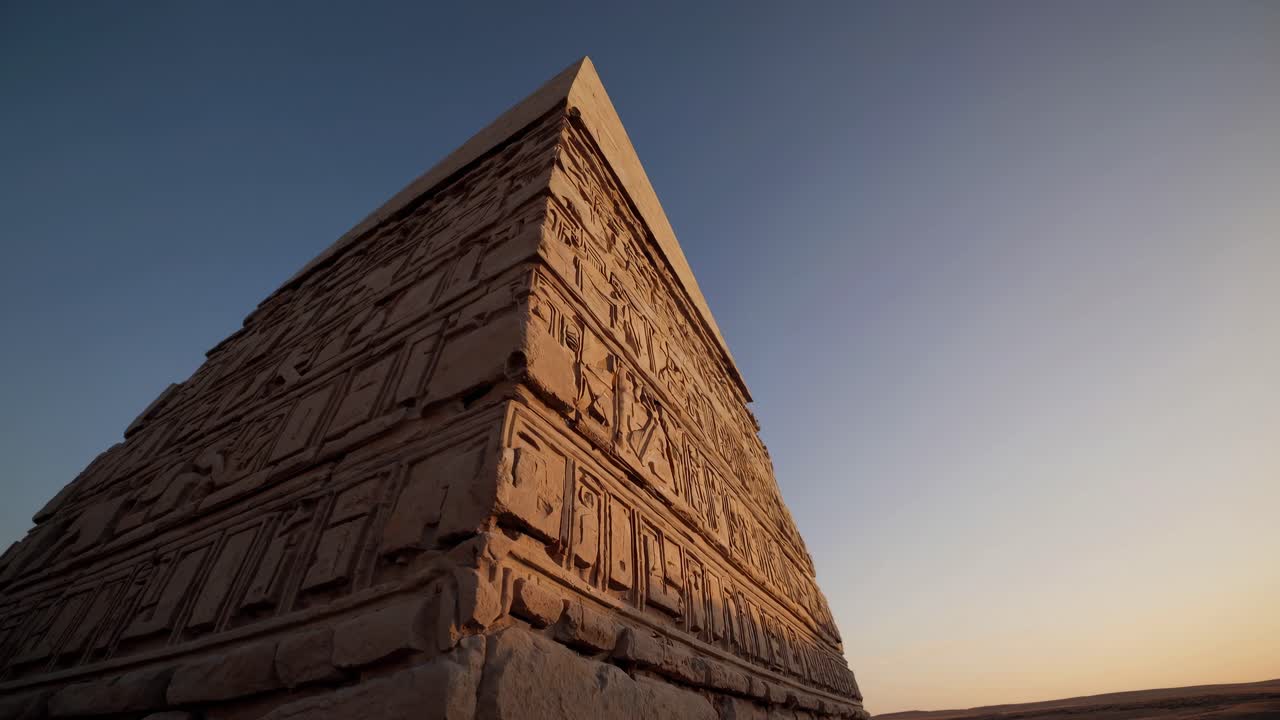 Low-angle video shot of an ancient pyramid against a clear sky, highlighting detailed carvings