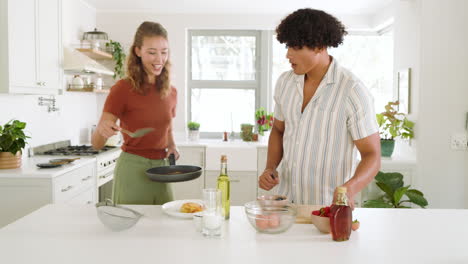 young man preparing fresh fruit salad in bright kitchen while woman cooking, at home