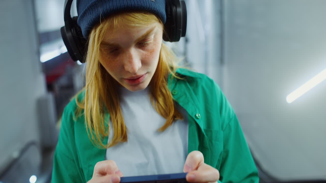 Woman with Headphones Playing on Mobile Phone