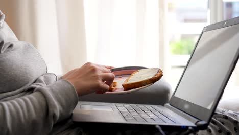 woman picking up a plate with a cheese toast while working from home on her laptop