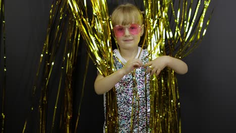 happy child dancing, playing, fooling around in shiny foil fringe golden curtain. little blonde kid