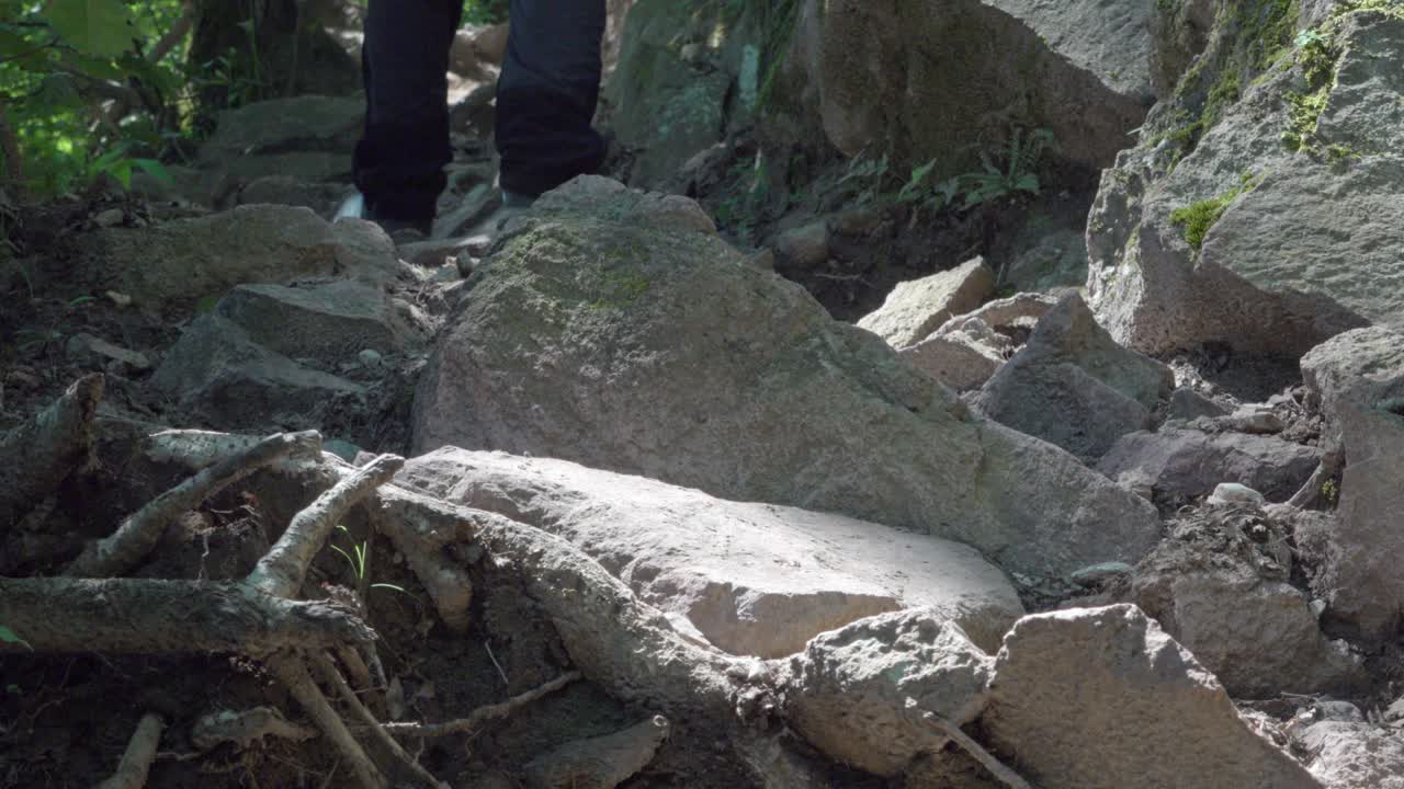 Feet in hiking boots climb a trail that leads over stony terrain
