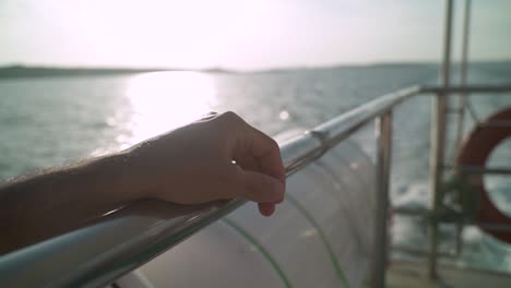 close up on a hand on a rail of a boat sailing in the ocean waters