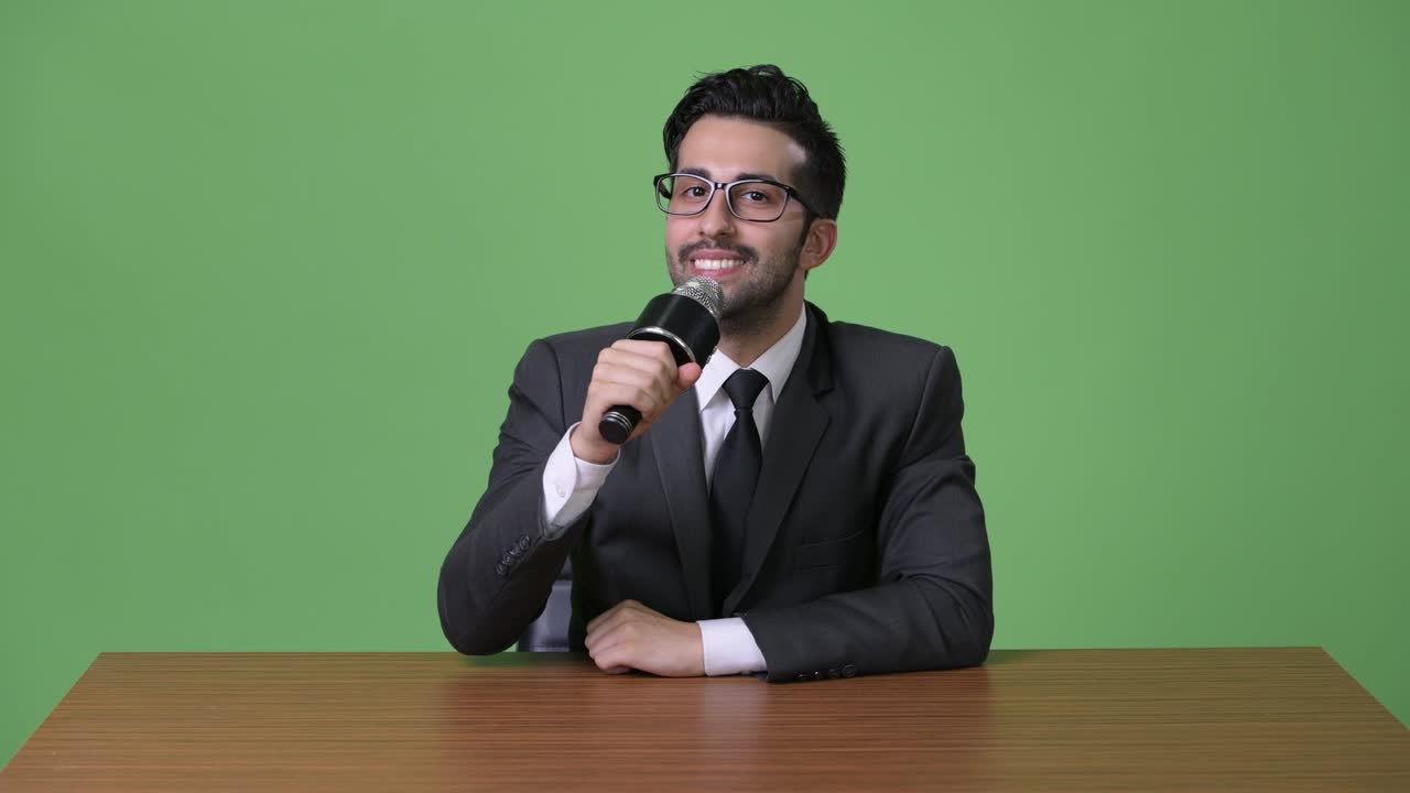 Young handsome bearded Persian businessman against green background