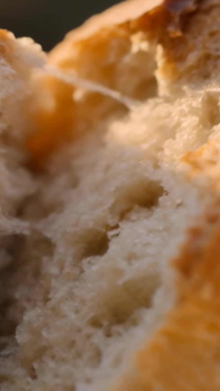Vertical video: Pressing seam with thumb, hand peeling open crusty loaf on counter showing crumb