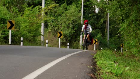 Asian-female-cyclist-biking-uphill-on-road-towards-camera-during-day,-Thailand