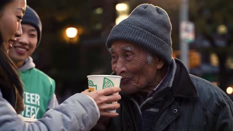 on a cool evening in the city, an elderly man shares a warm moment with young volunteers. their smiles brighten the atmosphere as they connect over a warm drink.