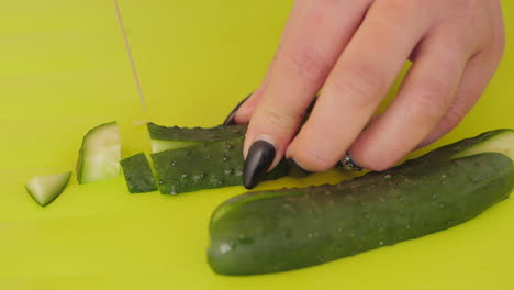 Mini-cucumber-being-sliced-into-smaller-pieces-with-knife-on-chopping-board