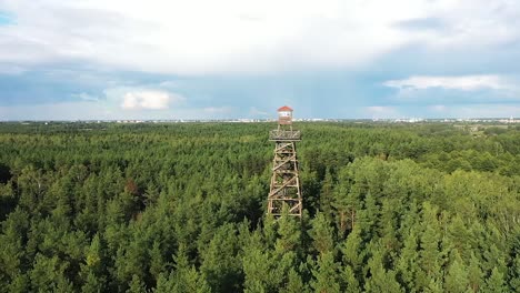 a drone circles a lookout tower deep in the forest as dark blue storm clouds gather above, sunbeams shining through with vivid color contrasts