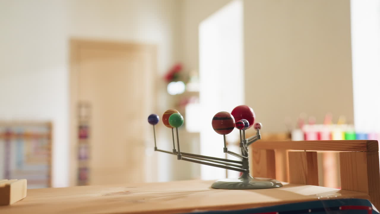 Close up of miniature planetary model displaying colorful orbits of nine planets under warm indoor light, spheres of varying sizes and hues represent solar system planets